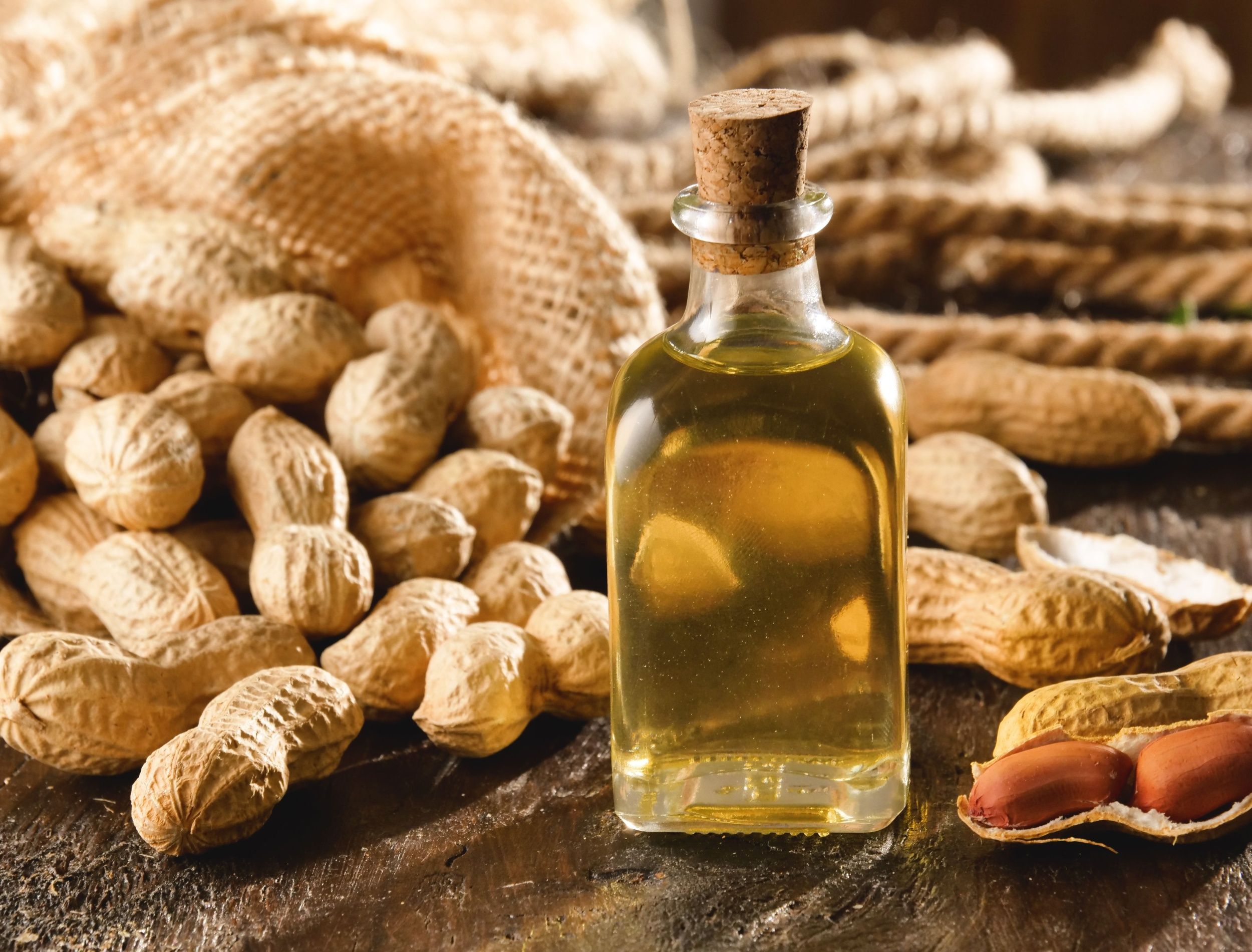 Rustic still life of a glass bottle of peanut oil surrounded by shelled and unshelled peanuts